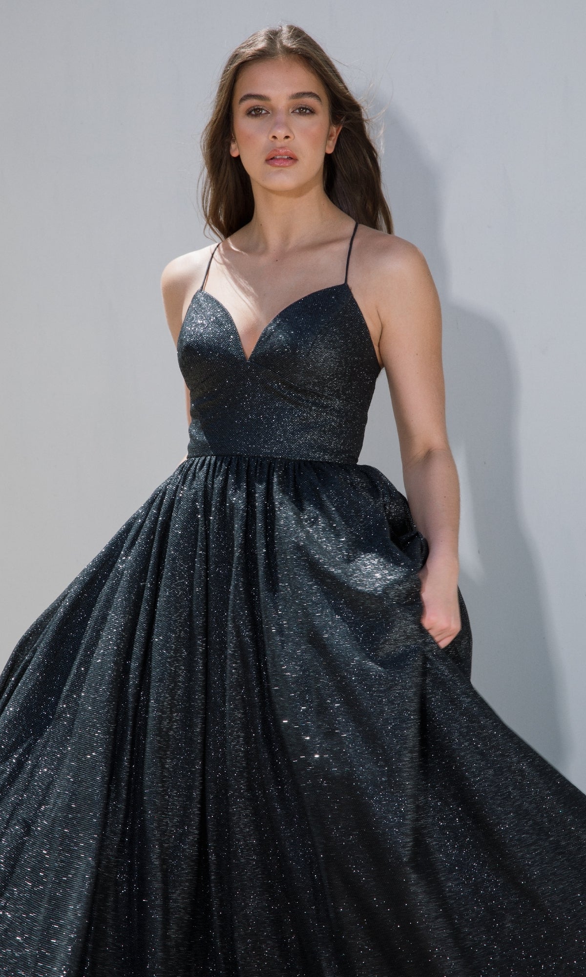 A woman models the Strappy-Back Glitter Prom Ball Gown (Eureka 9009), a sleeveless dark A-line dress with thin straps, against a plain light background.